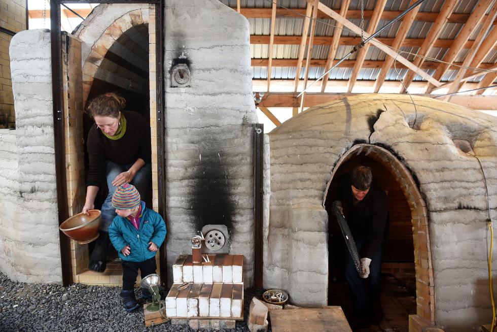 Becca, left, and Nathan Webb, right, remove shelving from their wood-fired kiln with some help from their daughter Zoe, 1, at their Two Potters business in Bethel, Vt. Wednesday, March 11, 2015. The couple completed the 30 foot kiln in 2012 after three years of work. Instead of glazing most of their work, the ash from the wood fire creates unpredictable patterns on the surface of their work. "It is very unknown from firing to firing," said Becca Webb. "The same piece in the same spot, you just don't know what's going to come out." (Valley News - James M. Patterson) Copyright Â© Valley News. May not be reprinted or used online without permission. Send requests to permission@vnews.com. - James M. Patterson | Valley News