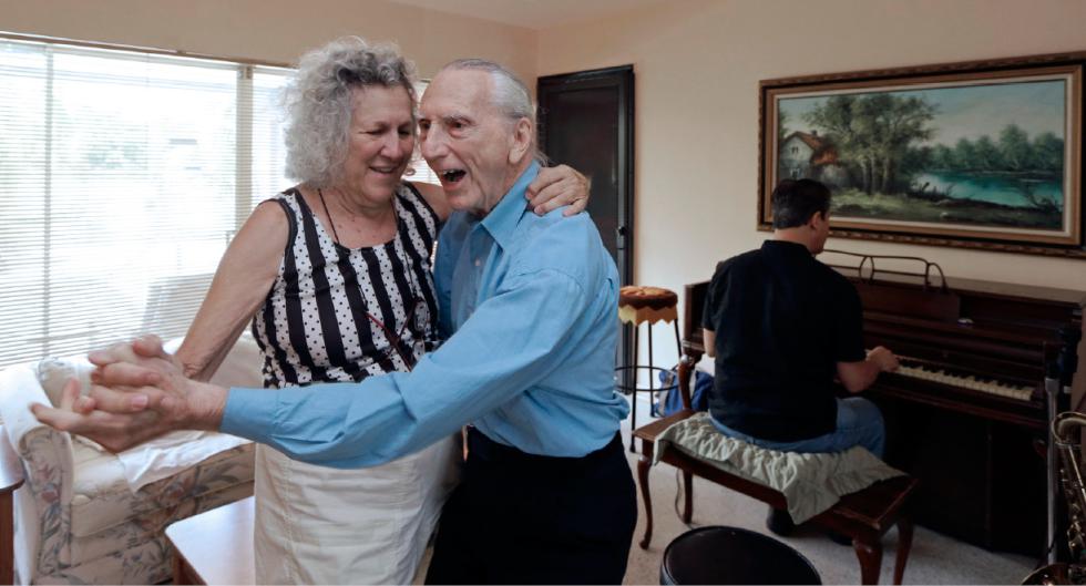 In this May 11, 2015 photo, Al Karp, right foreground, and his wife Saundra, left, dance to the music their son Larry, background, plays on the piano at their home in North Miami Beach, Fla. The trio performs old standards locally as the Karp Family to ease stress and help raise money to save their home from foreclosure. (AP Photo/Alan Diaz) - Alan Diaz | AP