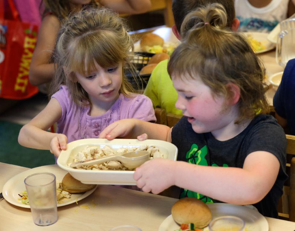 Rebekah Webb, left, shares a family-style meal with Zoe Turner during lunch with other five-year-olds at the Olathe Family YMCA in Olathe, Kan., Wednesday, June 24, 2015. As early childhood teachers lament toddlers too large to fit in playground swings, officials are mulling changes designed to make meals served to millions of kids in day care healthier.  (AP Photo/Orlin Wagner) - Orlin Wagner | AP