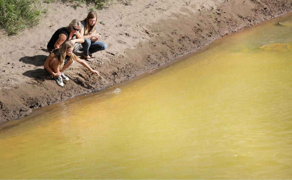 Kim Cofman and her daughters Acacia, 12, left, and Cayenne, 14, try to stir up sludge from the Gold King Mine that covers the bottom the Animas River on Saturday, Aug. 8, 2015, in Durango, Colo., near the 32nd Street Bridge but find the only way to disturb it is to dig into the yellow muck. Toxic waste is still flowing from the Gold King Mine. (Jerry McBride/The Durango Herald via AP) - Jerry McBride | THE DURANGO HERALD