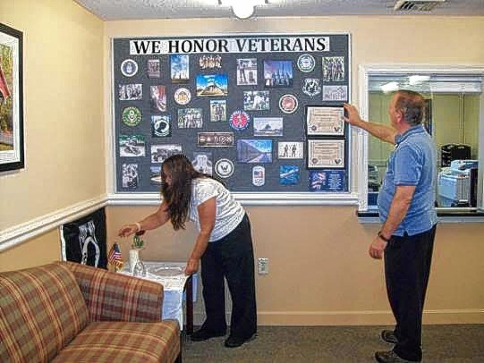 Lisa Brown, activity director at Hanover Terrace Health and Rehabilitation, and Randy Macdonald, coordinator of volunteer services for Visiting Nurse and Hospice of Vermont and New Hampshire, put the finishing touch on a We Honor Veterans display is in the front lobby area at Hanover Terrace. The program, a collaboration between the National Hospice and Palliative Care Organization and the Department of Veterans Affairs, focuses on improving care for veterans. The service of veterans who live at Hanover Terrace is acknowledged with a certificate placed over their bed. Allyson Delaney photograph - 