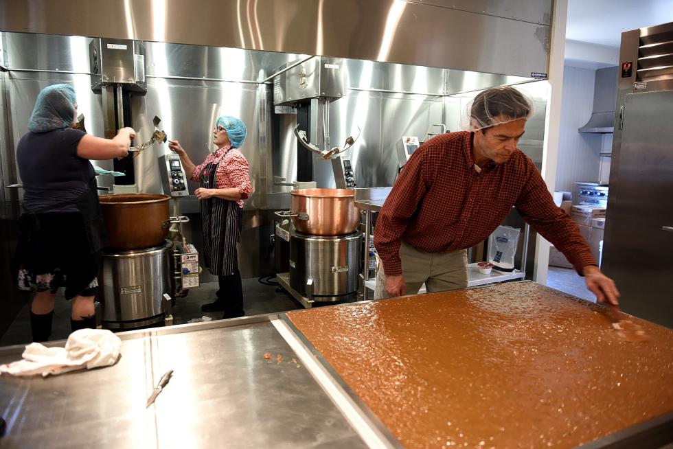 Red Kite Candy co-owner Mike McCabe spreads carmel with pecans on a cooling table at their new facility in Bradford, Vt., Nov. 4, 2015. Cleaning the kettle where the carmel was cooked is employee Laurie Lanctot, left, and co-owner Elaine McCabe.(Valley News - Jennifer Hauck) Copyright © Valley News. May not be reprinted or used online without permission. Send requests to permission@vnews.com. - Jennifer Hauck | Valley News