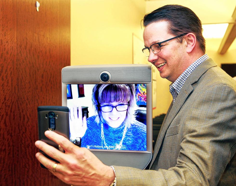 Amy Lamb, an app development consultant at Northwestern Mutual, has a severe poinsettia allergy, so she works at home during the holidays. Lamb, on screen, uses a robot that she controls from home to attend meetings at the office as seen on Tuesday, Dec. 29, 2015. Lamb's manager Tom Mullen takes a selfie of the two of them following a meeting. (Angela Peterson/Milwaukee Journal Sentinel/TNS) - Angela Peterson | Milwaukee Journal Sentinel