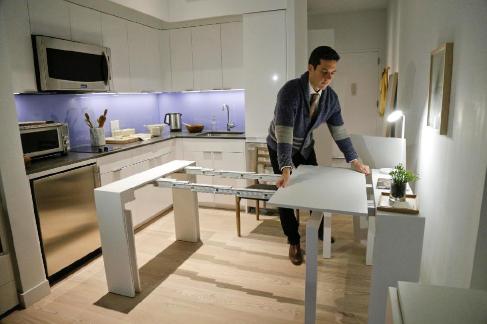 In this Dec. 22, 2015, photo, Stage 3 Properties co-founder Christopher Bledsoe demonstrates a desk that expands into a dining table that can seat up to 12 people inside one of the apartments at the Carmel Place building in New York. As the city-sponsored micro-apartment project nears completion, its setting an example for tiny dwellings that the nations biggest city sees as an aid to easing its affordable housing crunch. (AP Photo/Julie Jacobson) - Julie Jacobson | AP