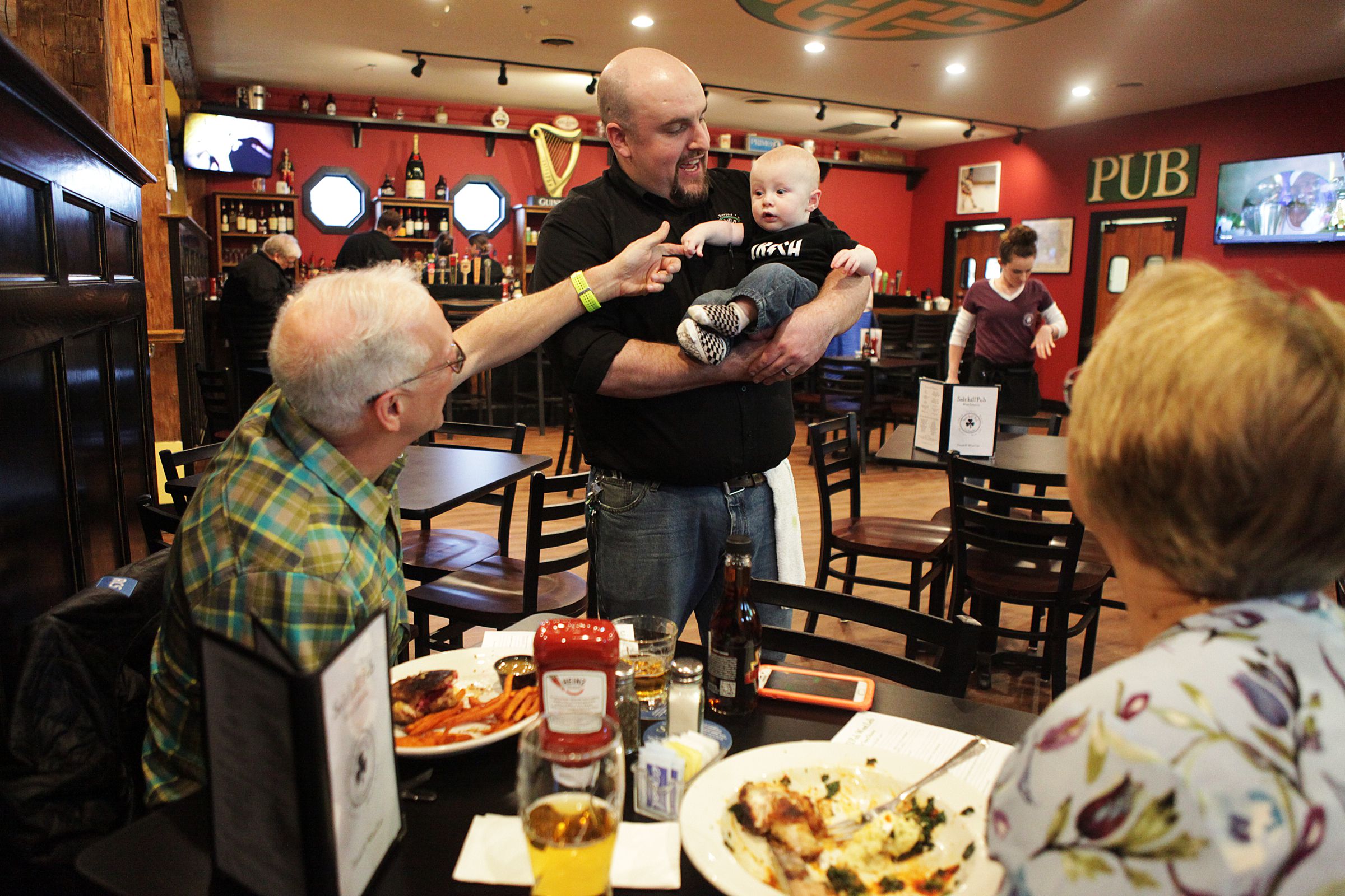 : PRE-PARTYEnfield resident Dave Albert, left, greets 6-month-old Benjamin McGary, held by his father, Josh McGary, the regional manager of Salt hill Pub, at the pre-opening party for the pub’s newest location in West Lebanon.