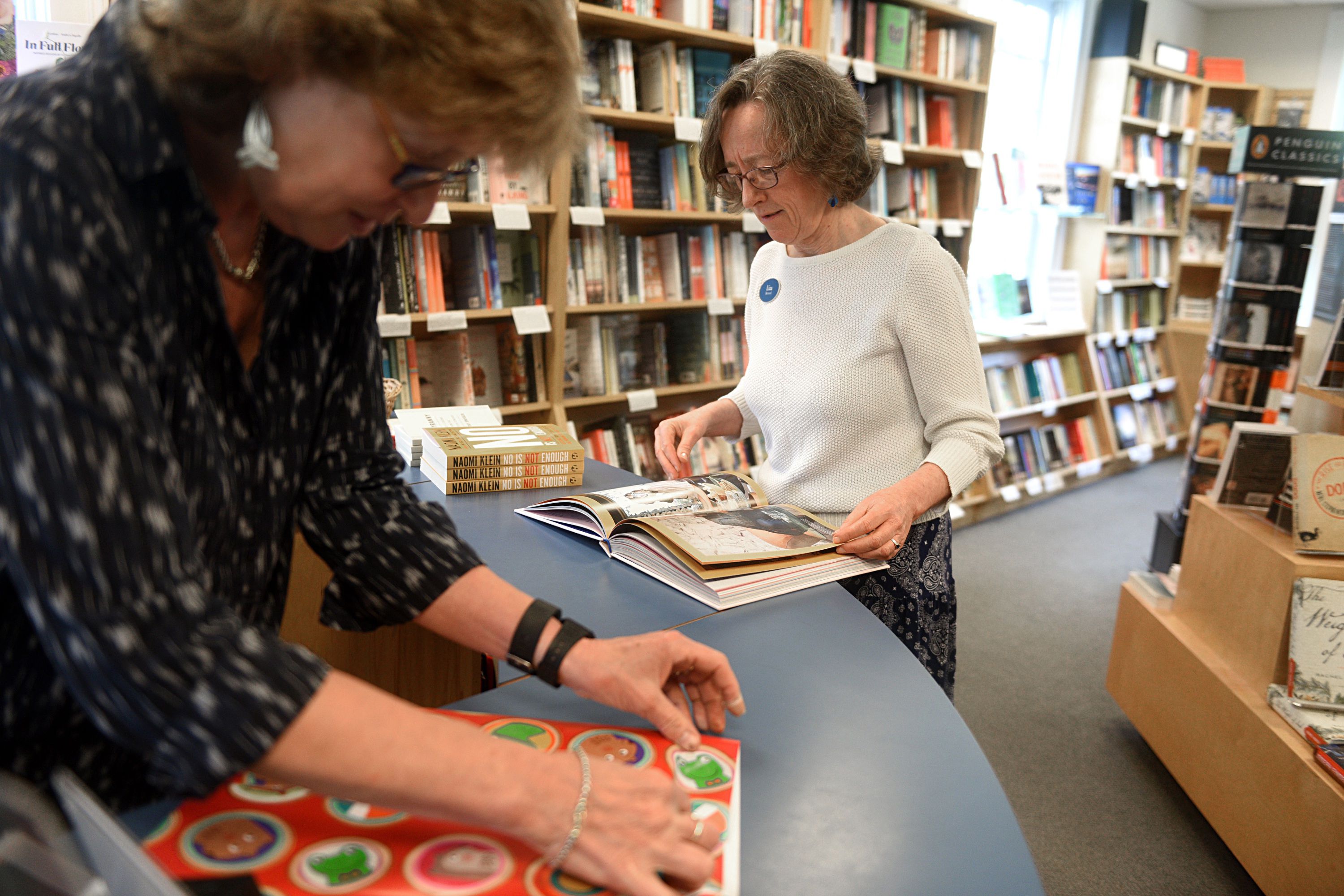Carin Pratt, left, wraps a gift for a customer as Liza Bernard pages through a book at the Norwich Bookstore on June 13, 2017, in Norwich, Vt. (Valley News - Jennifer Hauck) Copyright Valley News. May not be reprinted or used online without permission. Send requests to permission@vnews.com.