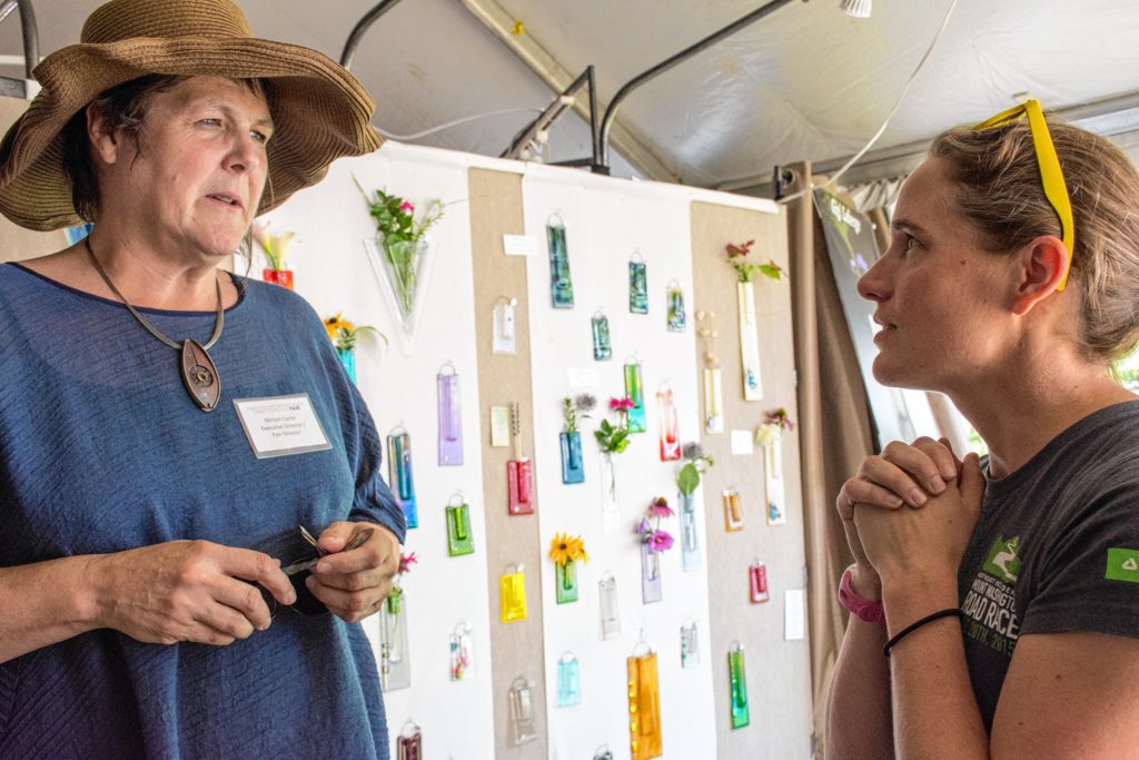 Miriam Carter, executive director of the League of New Hampshire Craftsmen, left, speaks with Amy Lane Rusiecki, right, of Deerfield, Mass., who has been visiting the craft fair since she was a child. Rusiecki's parents have a house in Sunapee and hitting the fair is an annual summer event. (Nancy Nutile-McMenemy photograph)