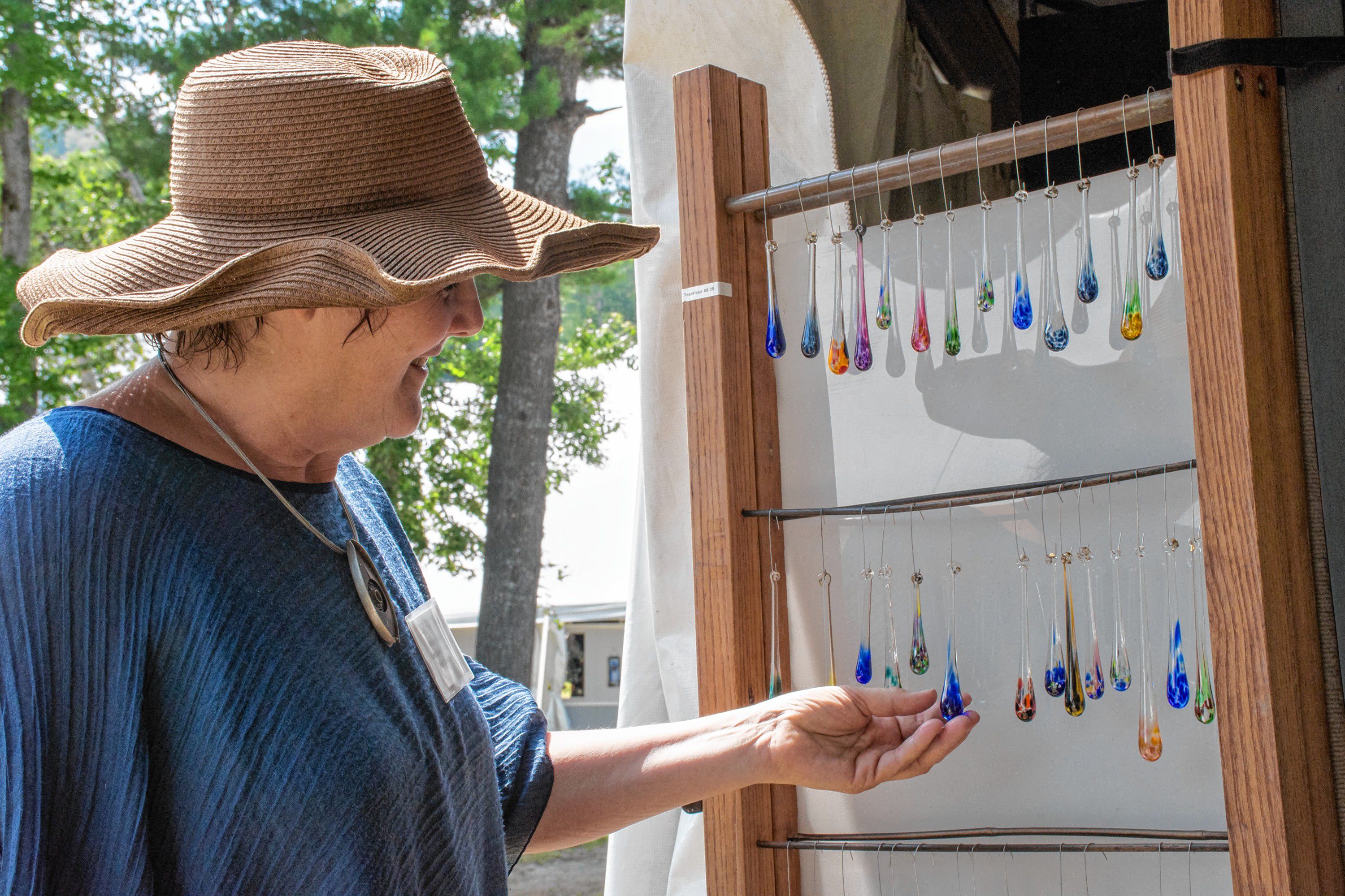 Miriam Carter, executive director of the League of New Hampshire Craftsmen, admires one of the "Sunapee Raindrops" created by glassblowers Harry and Wendy Besett, of Hardwick, Vt. (Nancy Nutile-McMenemy photograph)