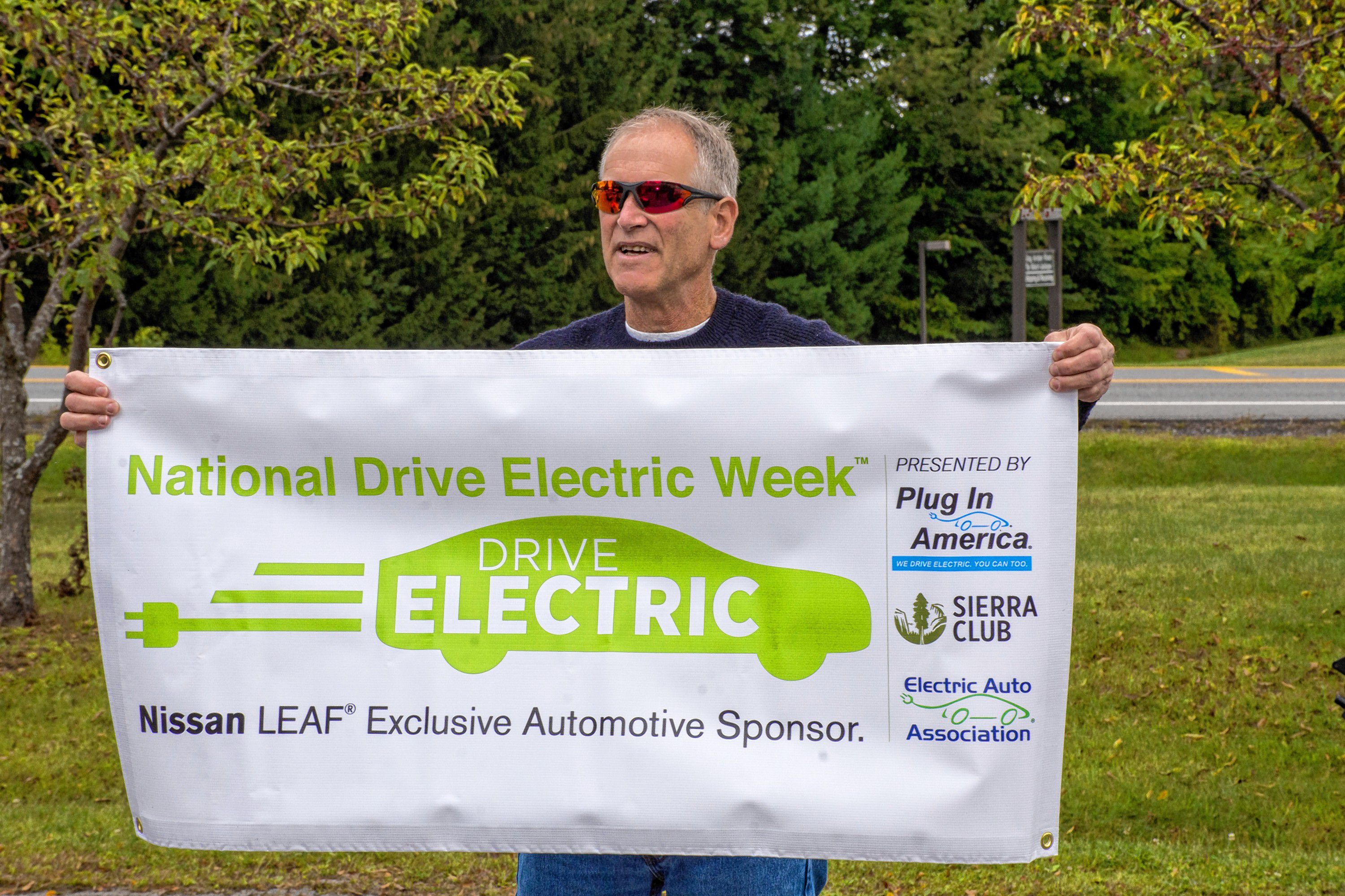 Jamie Hess, a member of the New London (N.H.) Energy Committee, holds one of the many banners that were on display at the second annual Upper Valley Electric Vehicle Expo on Sept. 9 at Dothan Brook School in Hartford, Vt. (Nancy Nutile-McMenemy photograph)