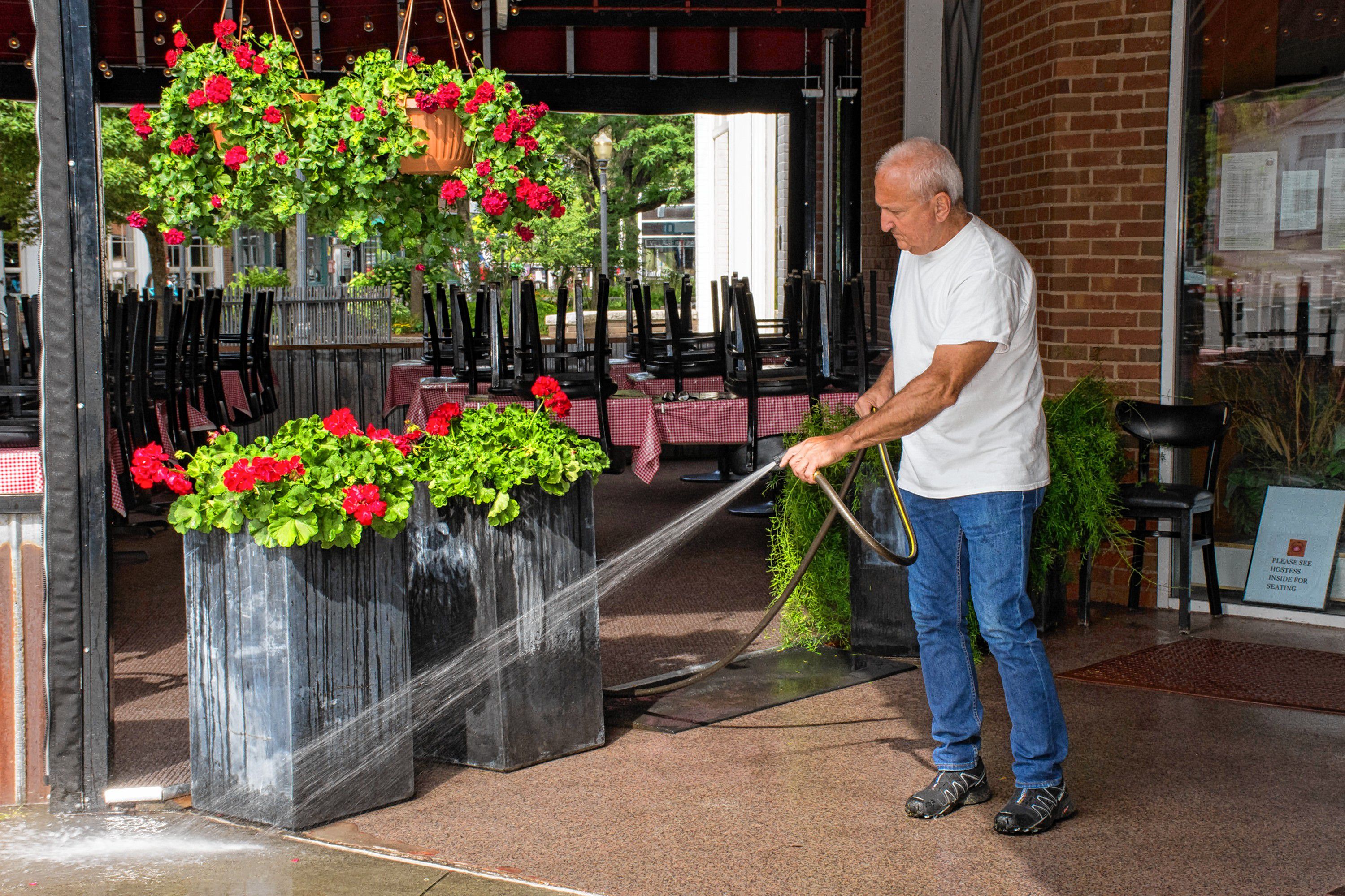 Robert Meyers, owner of Three Tomatoes Trattoria in Lebanon, N.H., washes down the sidewalk before opening for lunch -- just like restaurants in the old country. (Nancy Nutile-McMenemy photograph)