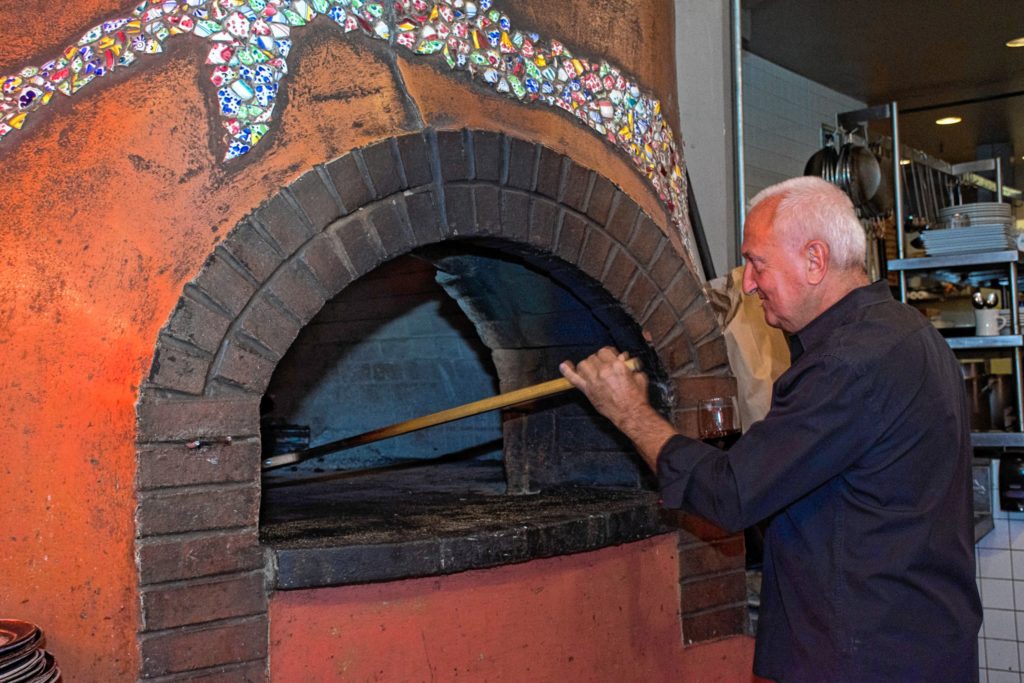 The wood fired oven at Three Tomatoes Trattoria in Lebanon, N.H., gets a little more prodding from owner Robert Meyers. (Nancy Nutile-McMenemy photograph)