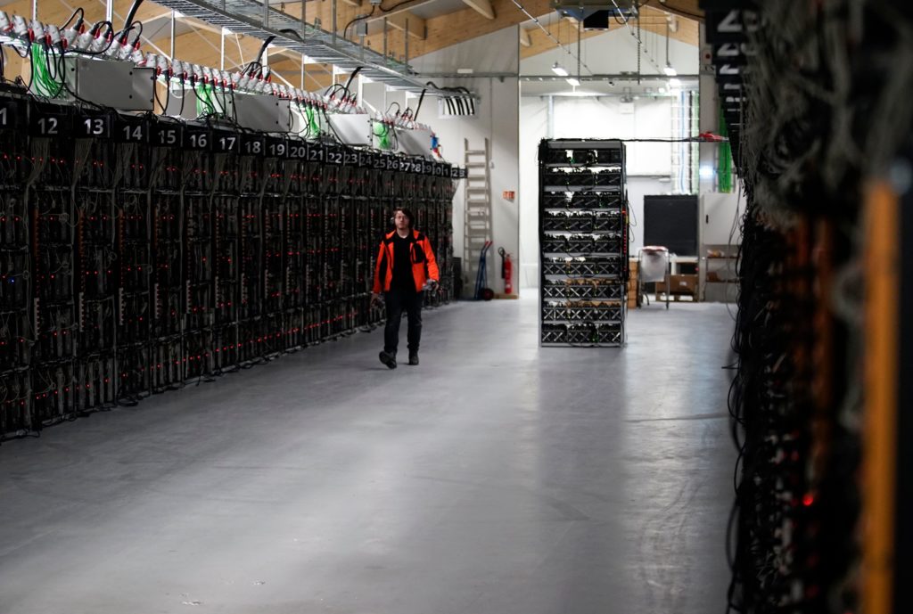 FILE _ In this file photo taken on Jan. 17, 2018, a worker walks along a row of computer rigs that run around the clock 'mining' bitcoin inside the Genesis Mining cryptocurrency mine in Keflavik, Iceland. A prisoner in Iceland suspected of masterminding the theft of about 600 computers used to mine bitcoin has managed to escape custody and flee the remote North Atlantic nation on a passenger plane. Police said surveillance footage showed a suspect they identified as Sindri Thor Stefansson boarding a passenger plane to Sweden on Tuesday April 17, 2018. (AP Photos/Egill Bjarnason, File)