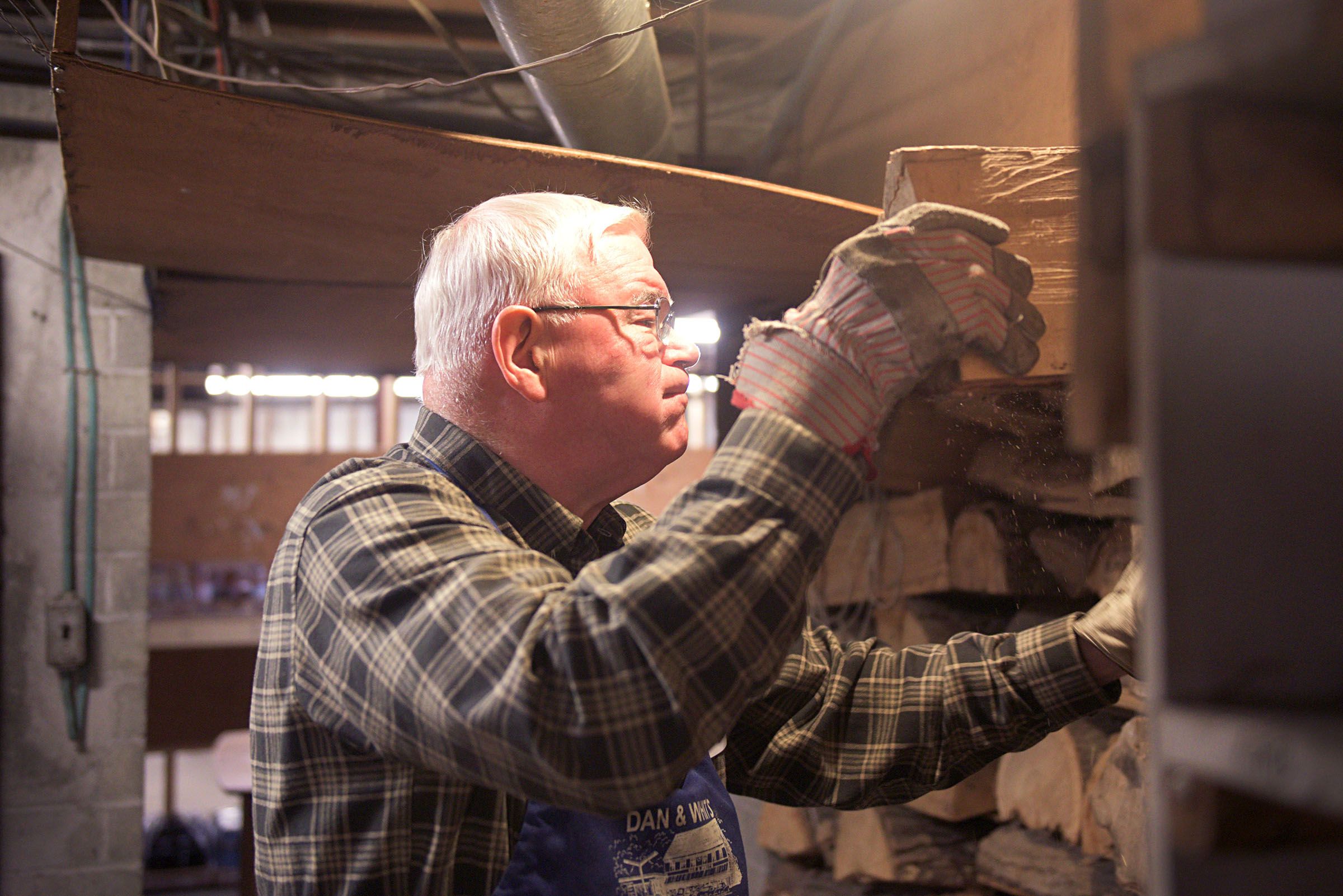 George Fraser, co-owner of Dan & Whit's General Store, grabs fuel for the woodstove in the store's basement in Norwich, Vt., on Jan. 7, 2019. Fraser is the eldest generation of this multigenerational area family business. (Valley News - Joseph Ressler) Copyright Valley News. May not be reprinted or used online without permission. Send requests to permission@vnews.com.