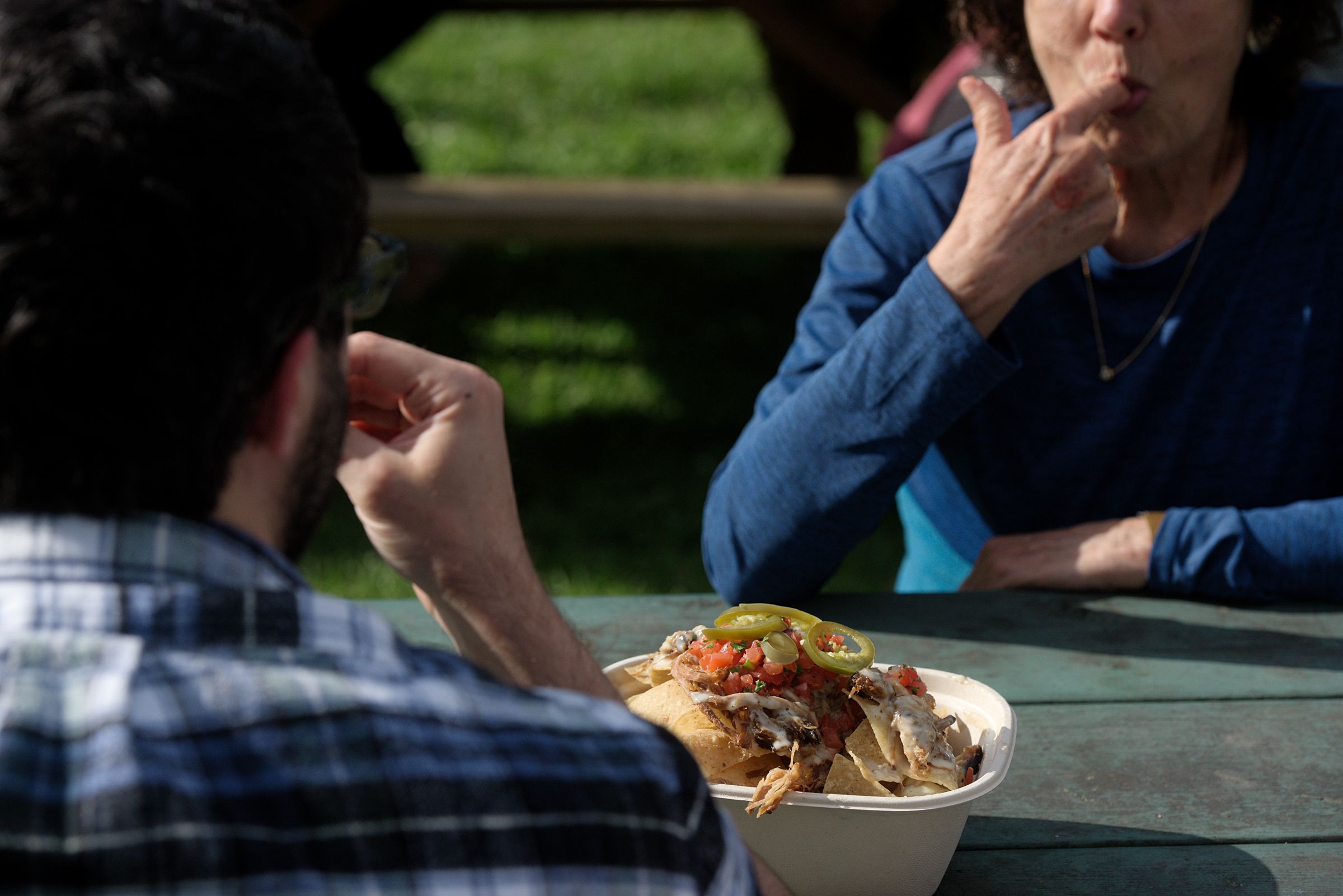 Peggy Tavare, of Berkeley, Calif., cleans her fingers while eating pulled pork nachos from The Box with her son Ian Tavare, left, of Lebanon, N.H., during the Lebanon, (N.H.) Food Truck Festival in Colburn Park, Friday, June 21, 2019. (Valley News - James M. Patterson) Copyright Valley News. May not be reprinted or used online without permission. Send requests to permission@vnews.com.