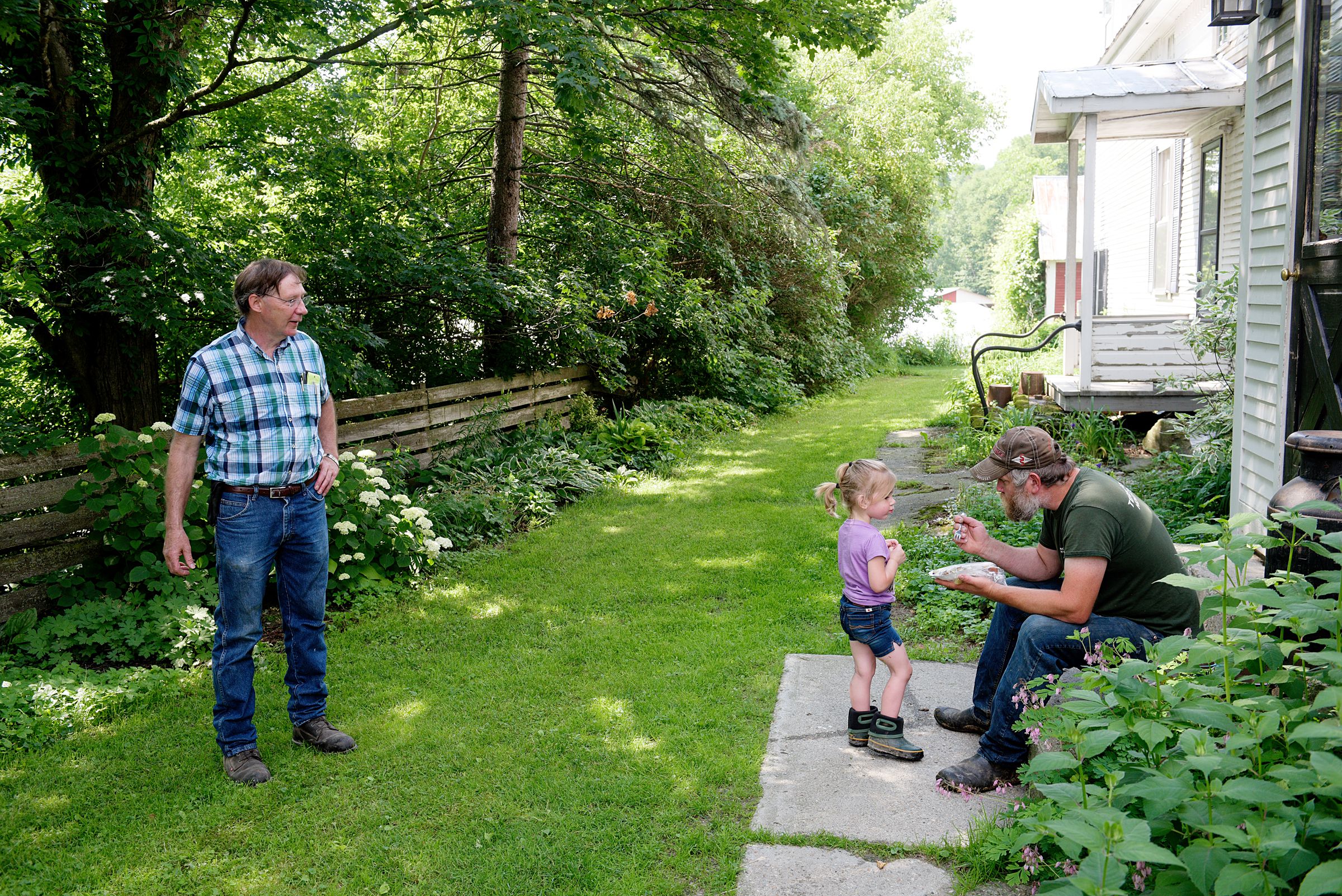 IBA dealer John Kerr, left, talks with farmer Dave Kennett, and his daughter Cecilia, 3, of Liberty Hill Farm in Rochester, Vt., before continuing his route Wednesday, July 3, 2019. (Valley News - James M. Patterson) Copyright Valley News. May not be reprinted or used online without permission. Send requests to permission@vnews.com.