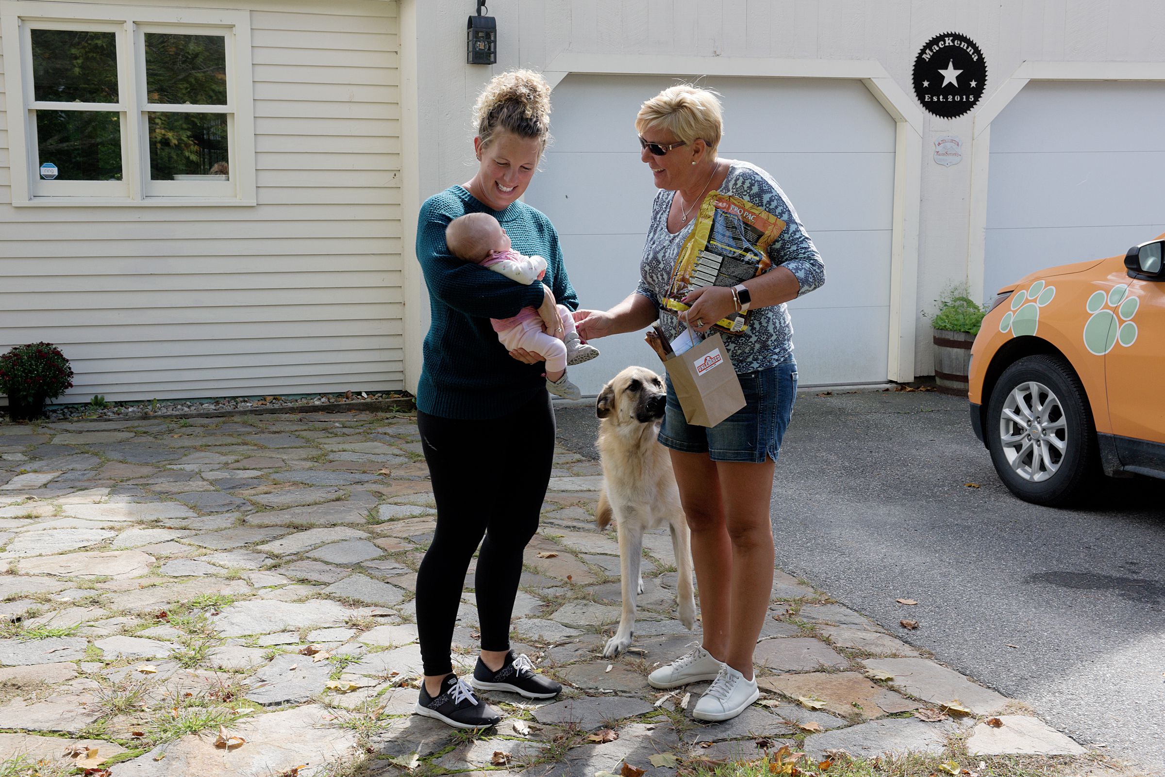 Max, a German shepherd, sniffs at a bag of treats, part of a pet food delivery from Unleashed, as the store owner Penny Murano, right, is greeted by Katie MacKenna and her baby Madison in New London, Wednesday, Sept. 25, 2019. Murano added a pet food subscription delivery service to her business in 2018 and is testing the water with same-day deliveries. (Valley News - James M. Patterson) Copyright Valley News. May not be reprinted or used online without permission. Send requests to permission@vnews.com.