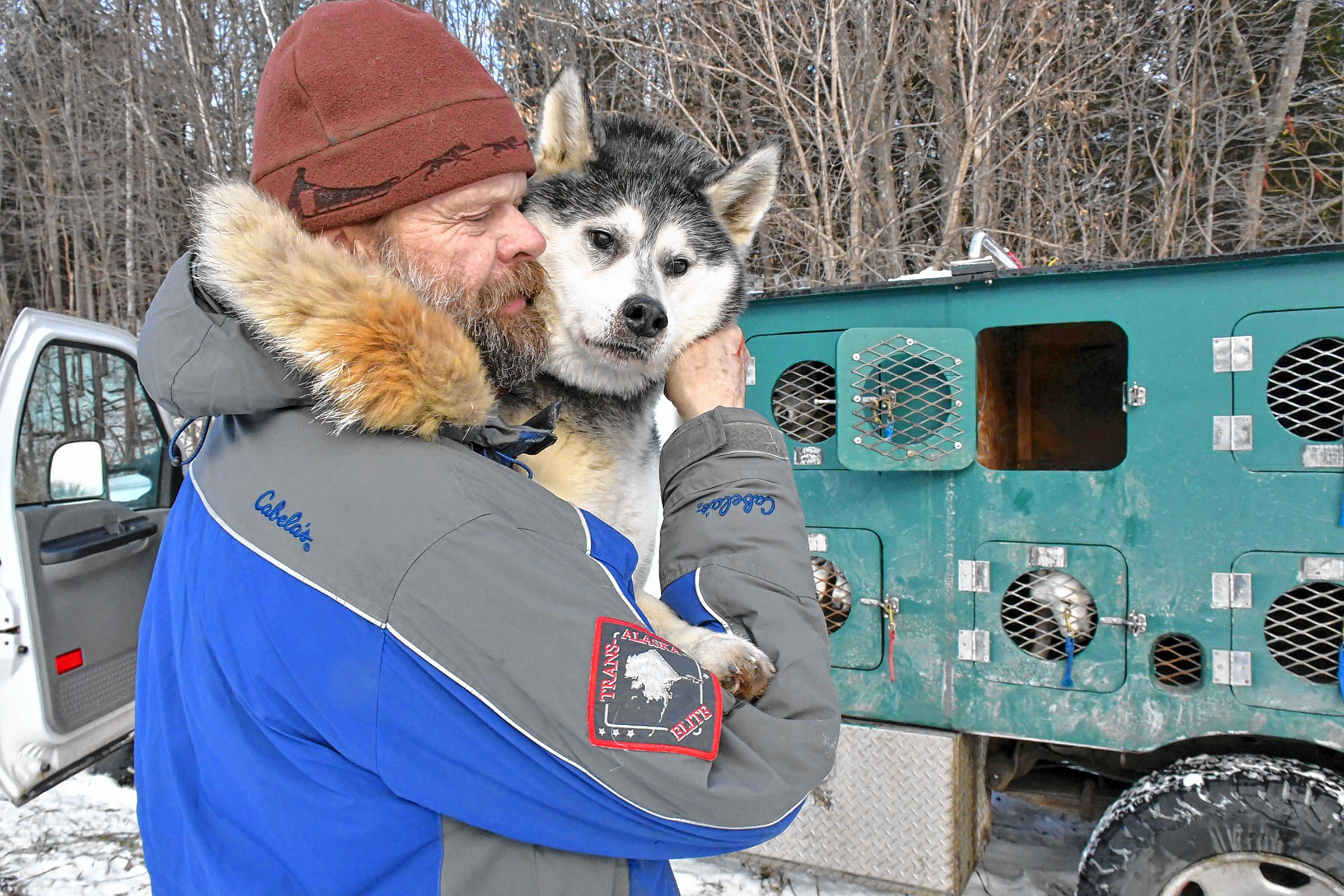 Alex MacLennan of Windsor, Vt., who is co-owner of Braeburn Siberians, pauses to spend a moment with Anakin, the patriarch of his sled dog team while lifting him down from his truck kennel in Claremont, N.H., on Sun. Dec. 22, 2019. Anakin is the grandfather of most of MacLennan's dogs and though nearly blind still likes to pull sleds while being guided by the dog harnessed next to him. (Rick Russell photograph)