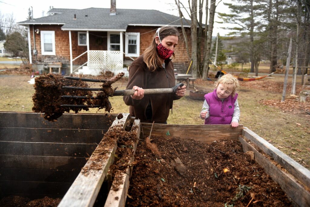 With steam pouring out, Jen Murphy of Willow Tree Community Compost moves her youngest compost to the next level of breakdown at her home in Wilder, Vt., on Thursday, March, 25, 2021. Her daughter Willow, who turns 3 in April, holds a sprout found growing in the bin. (Valley News - Jennifer Hauck) Copyright Valley News. May not be reprinted or used online without permission. Send requests to permission@vnews.com.