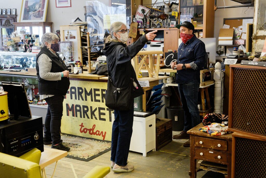 Marge Audet, of Bradford, left, and Cindy Perry, of Thetford, middle, both admired pieces of natural wood furniture by the same maker at Consign and Design owned by Chris Lin, right, in West Lebanon, N.H., Friday, March 26, 2021. Lin sells antiques and items he has collected while “picking” throughout New England on the ground floor of the store and has two floors of consignment booths above. “I’m finding everything I want today,” said Perry, who was outfitting a house she owns for short-term vacation rentals. “I’m getting what I need without shopping online. I’m sick of shopping online.” (Valley News - James M. Patterson) Copyright Valley News. May not be reprinted or used online without permission. Send requests to permission@vnews.com.