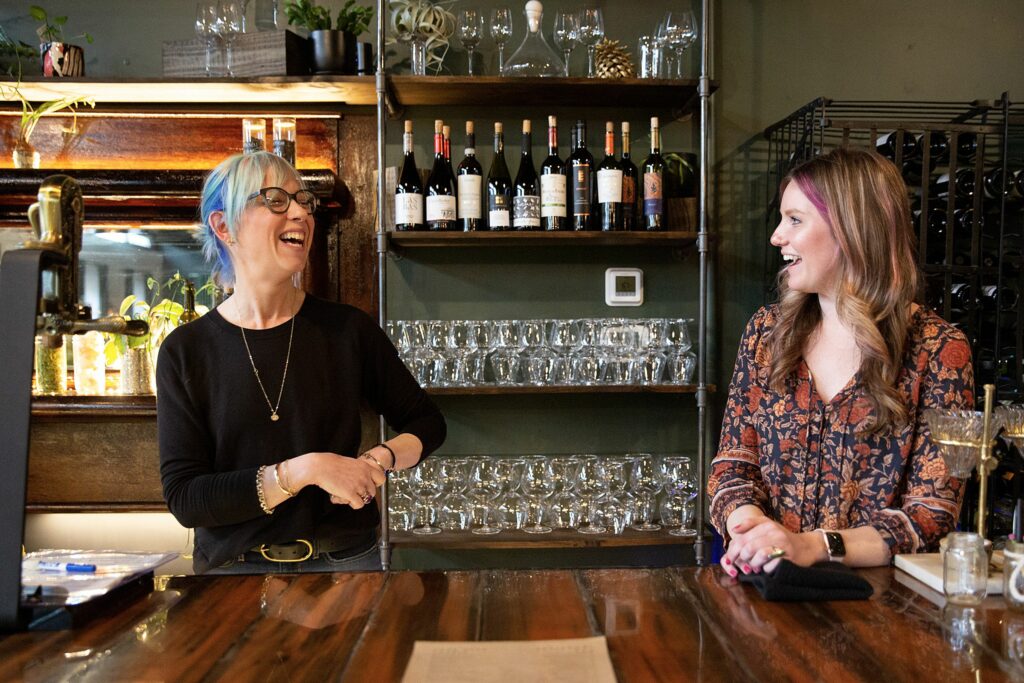 Putnam’s vine/yard owner Kelsey Rush, left, laughs as she talks with bartender Hunter Wilson at the wine bar in White River Junction, Vt., on Thursday, March 23, 2023. Rush said that her goal with the space was to create a place where she would like to spend time that is comfortable and inviting to customers. (Valley News / Report For America - Alex Driehaus) Copyright Valley News. May not be reprinted or used online without permission. Send requests to permission@vnews.com.