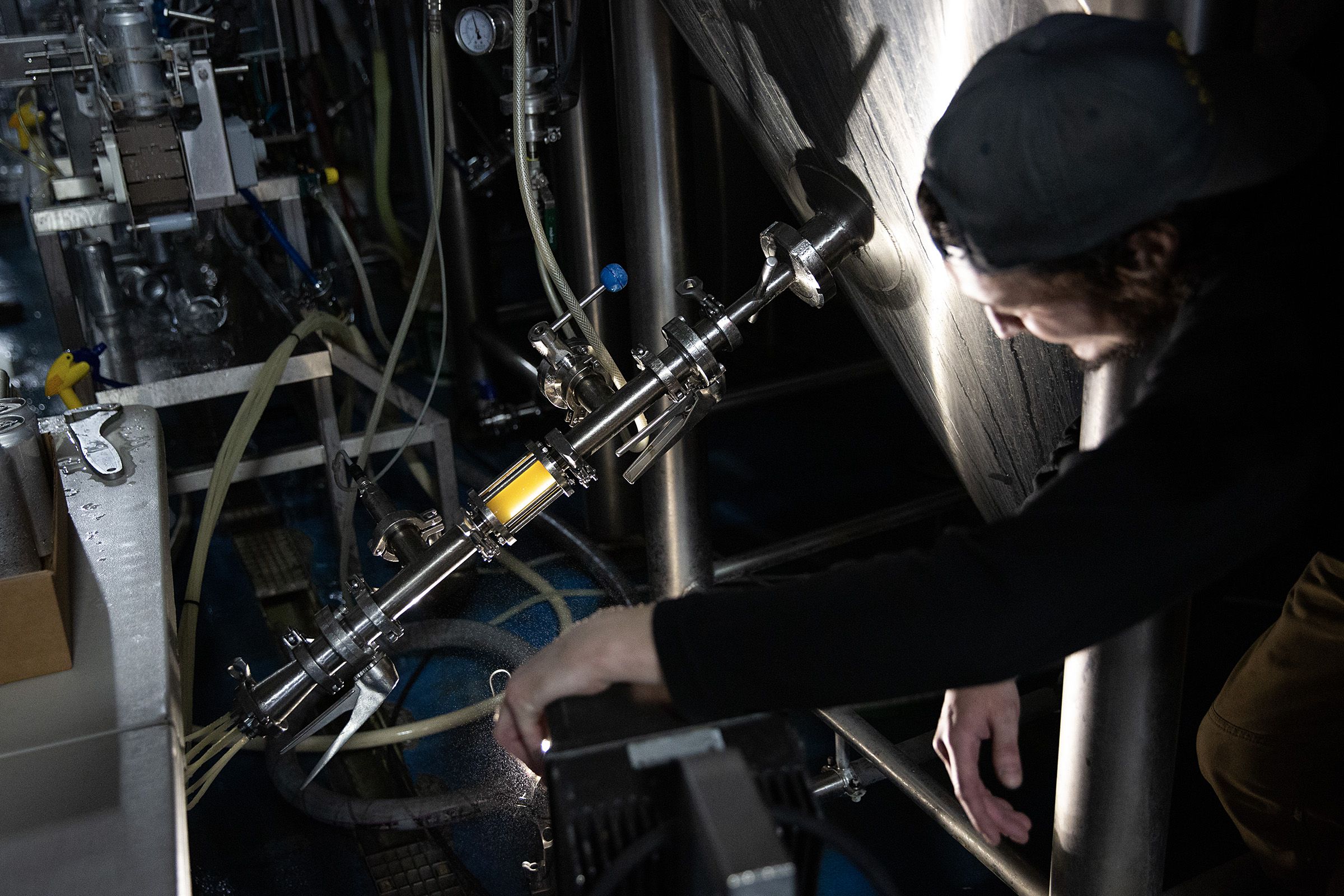 Sam Clemens adjusts brewing equipment while a light illuminates beer as it runs from a tank into canning equipment so it can be monitored for quality at River Roost Brewery in White River Junction, Vt., on Tuesday, March 28, 2023. (Valley News / Report For America - Alex Driehaus) Copyright Valley News. May not be reprinted or used online without permission. Send requests to permission@vnews.com.
